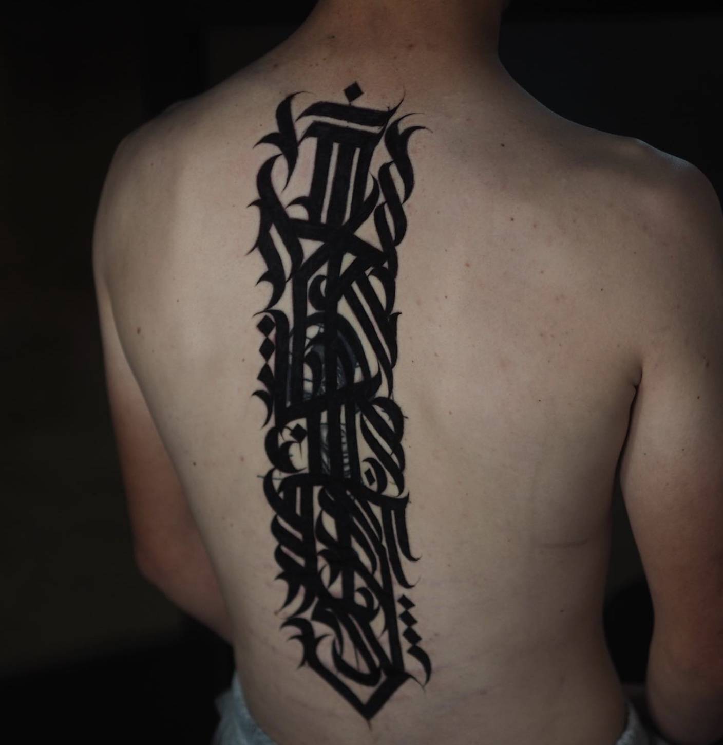 Back of head tattoo featuring detailed calligraphic lettering extending to upper back